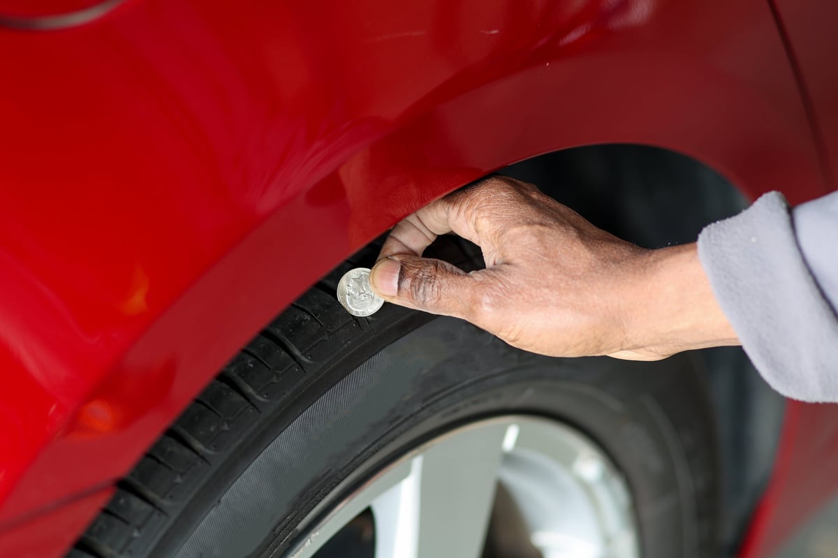 A black African-American man holding a coin in his hand to measure a tire tread on a vehicle