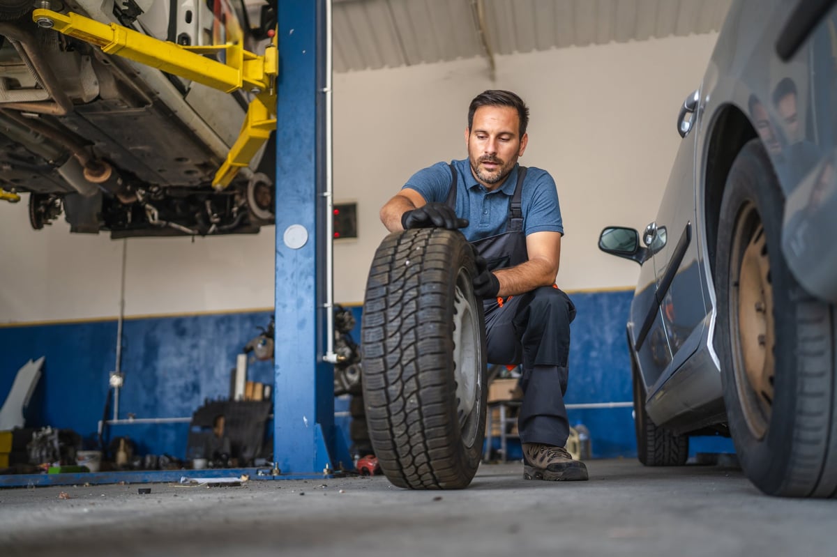 A focused car mechanic expertly handles a car tire in a modern auto repair shop, highlighting the precision and skill required in automotive maintenance and repair work