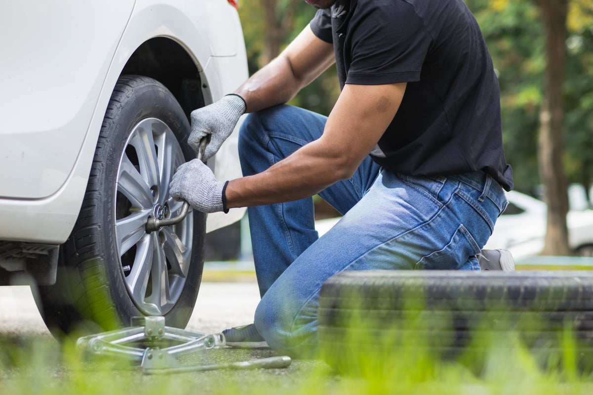 Mechanic preparing equipment and a spare tire to change the tire of a car that had a flat tire during a journey.