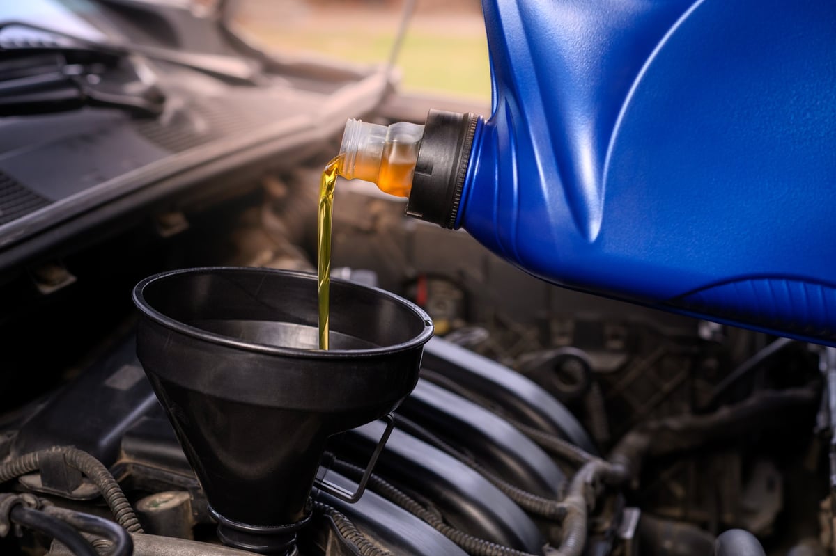 Close-up of motor oil being poured from canister via a funnel into a car engine. Car maintenance concept.