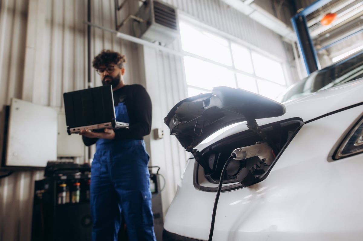 Male mechanic using laptop for diagnostic on electric vehicle in auto service center