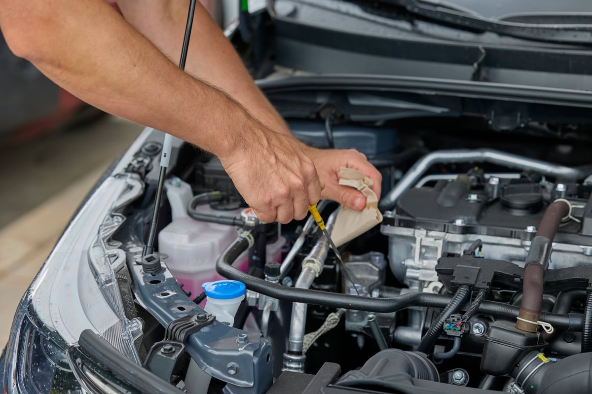 Man checking engine oil level in a car during routine maintenance inspection.